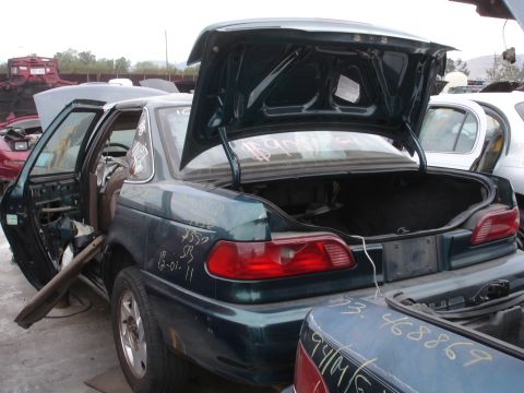 1993 Ford Taurus - This dark green sedan is in a junkyard, with its trunk and driver's door open, showing signs of wear and tear.