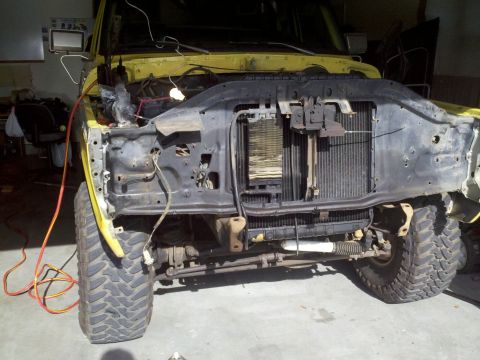 1978 Ford Bronco - The front end of a yellow SUV is disassembled, revealing the radiator and engine bay components.
