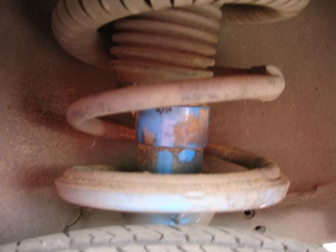 1993 Ford Taurus - Close-up view of a vehicle's suspension strut and coil spring, showing a blue painted cylinder with rust.