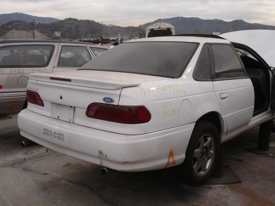 White 1993 Ford Taurus sedan with a spoiler and SHO badging, rear view, in a junkyard