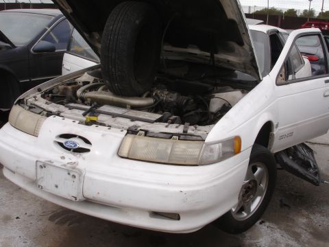 1993 Ford Taurus - Front view of a 1993 Ford Taurus with its hood open and a spare tire placed inside the engine compartment.