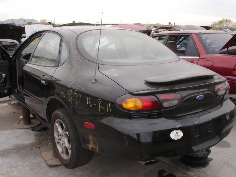 1993 Ford Taurus - This black 1993 Ford Taurus sedan is seen from the rear in a junkyard with other vehicles.