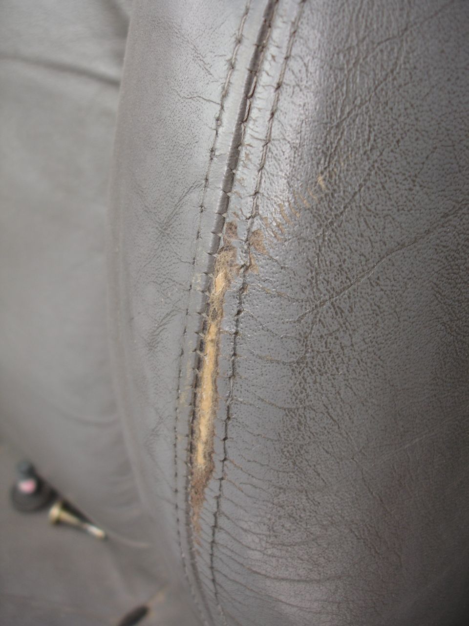 Dark gray leather car seat with a long tear exposing padding, showing stitching detail