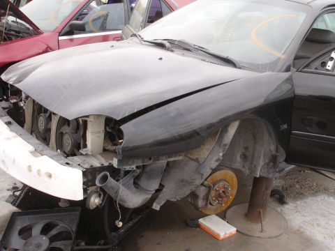 1993 Ford Taurus - Front view of a black 1993 Ford Taurus in a junkyard, missing its bumper and hood.