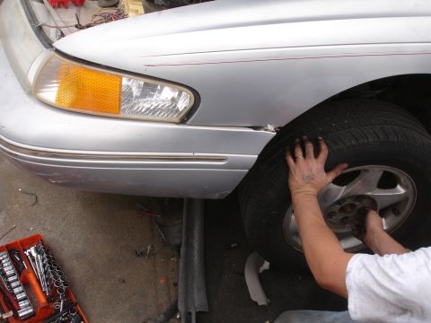 1993 Ford Taurus - A person works on the front wheel of a silver sedan, which appears to be a 1995 model based on its body style.
