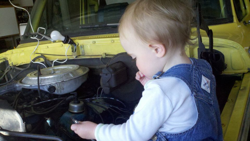 Yellow 1978 Ford Bronco engine bay with a toddler inspecting the motor