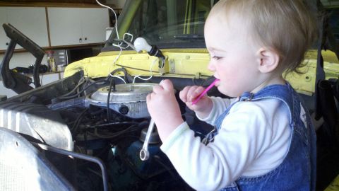 1978 Ford Bronco - A toddler plays with tools in the engine bay of a yellow vehicle.