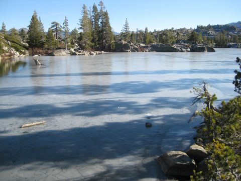 1986 Ford Bronco - A frozen lake is surrounded by rocky terrain and pine trees under a clear blue sky.