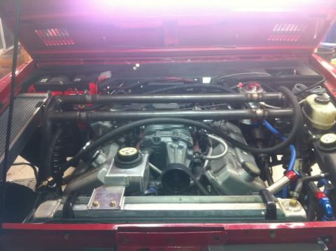 1976 Ford Bronco - Customized engine bay a prominent supercharger and roll cage, with visible "Supermotors.net" branding.