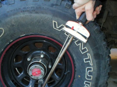 1989 Ford Bronco - A hand uses a beam-style torque wrench with a dial gauge to tighten lug nuts on a black steel wheel with a red pinstripe, mounted with a 33…