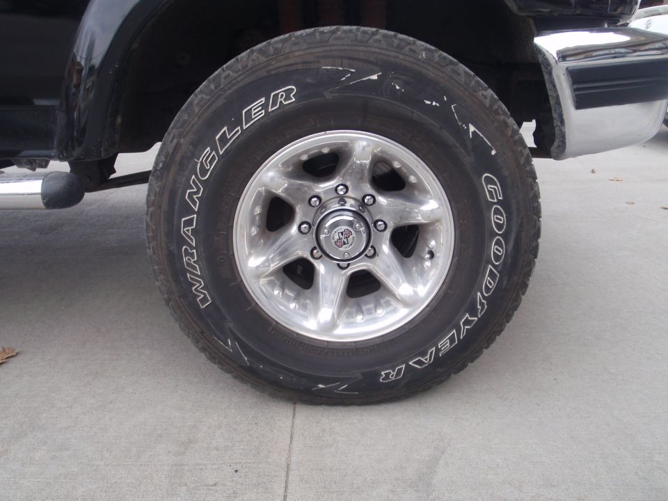 Close-up of a Goodyear Wrangler tire on a vehicle's front wheel. Chrome bumper visible