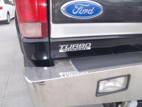 1994 Ford Bronco - Rear view of a black Ford truck with a "Turbo Diesel" emblem and chrome bumper, parked next to a white car.