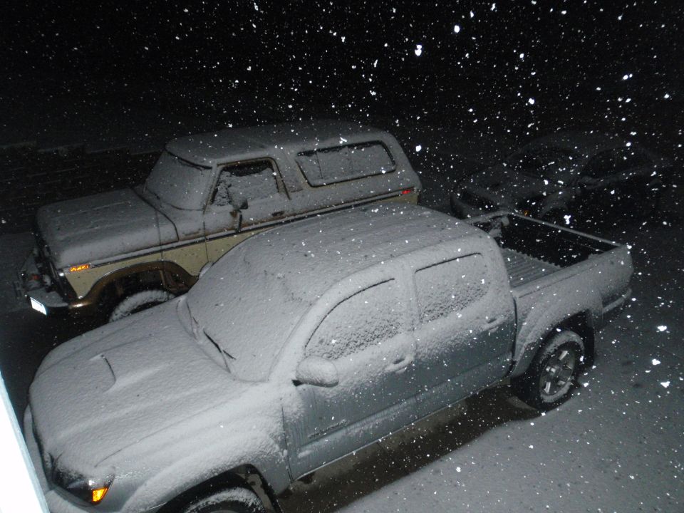 1978 Ford Bronco and a modern pickup truck covered in snow at night