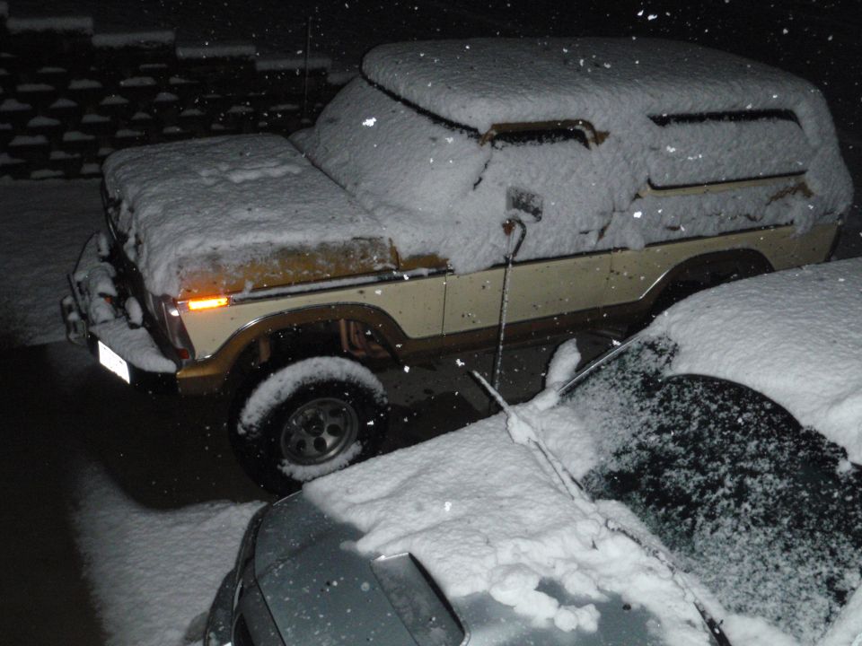1978 Ford Bronco, beige and brown, covered in snow, parked next to another snow-covered car