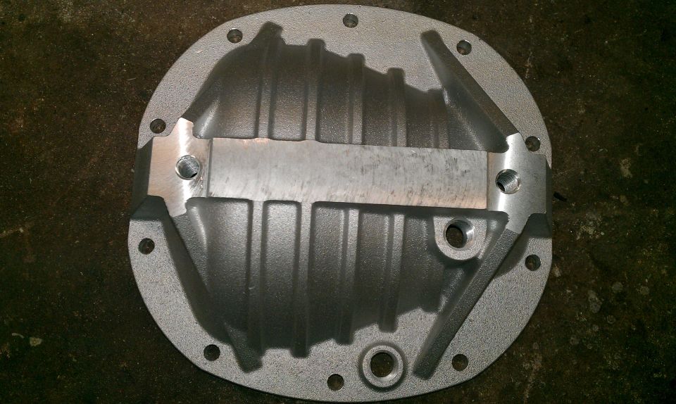 Differential cover with fins and a metal brace, bolted to a dark surface