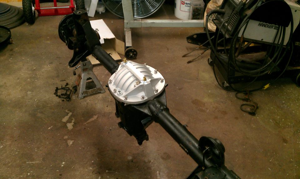 Rear axle assembly with a silver differential cover, sitting on jack stands in a garage
