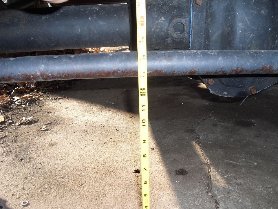 Measuring tape against rusty metal bar and vehicle axle housing