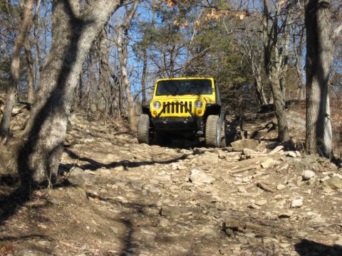 2005 Jeep Wrangler - A yellow 2005 Jeep Wrangler navigates a challenging rocky path through a wooded area.