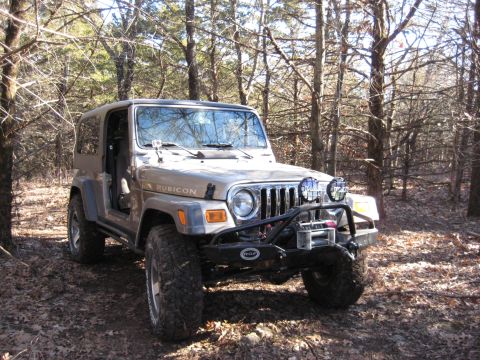 2005 Jeep Wrangler - A tan Jeep Wrangler Rubicon is parked on a dirt path surrounded by trees in a wooded area.