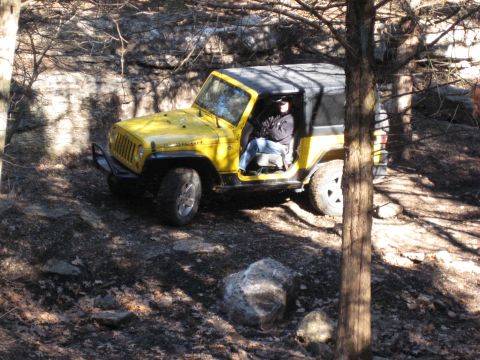 2005 Jeep Wrangler - A yellow 2005 Jeep Wrangler navigates a challenging off-road path with rocks and trees.