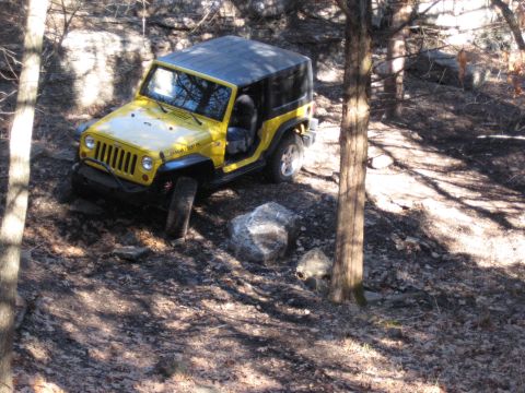 2005 Jeep Wrangler - A yellow Jeep Wrangler navigates a rocky, wooded trail.
