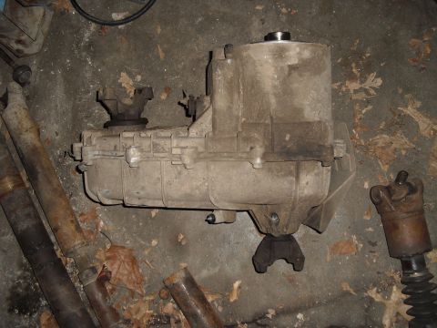1986 Ford Bronco - Transfer case and associated driveshafts are shown lying on a concrete surface with scattered leaves.