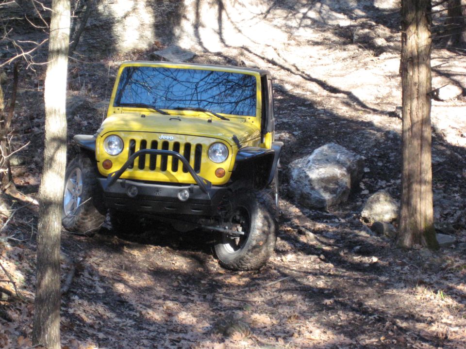Yellow Jeep Wrangler driving on a dirt trail with trees and rocks