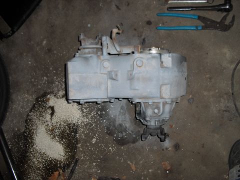 1986 Ford Bronco - Transfer case shown on a workshop floor, surrounded by sawdust and tools.