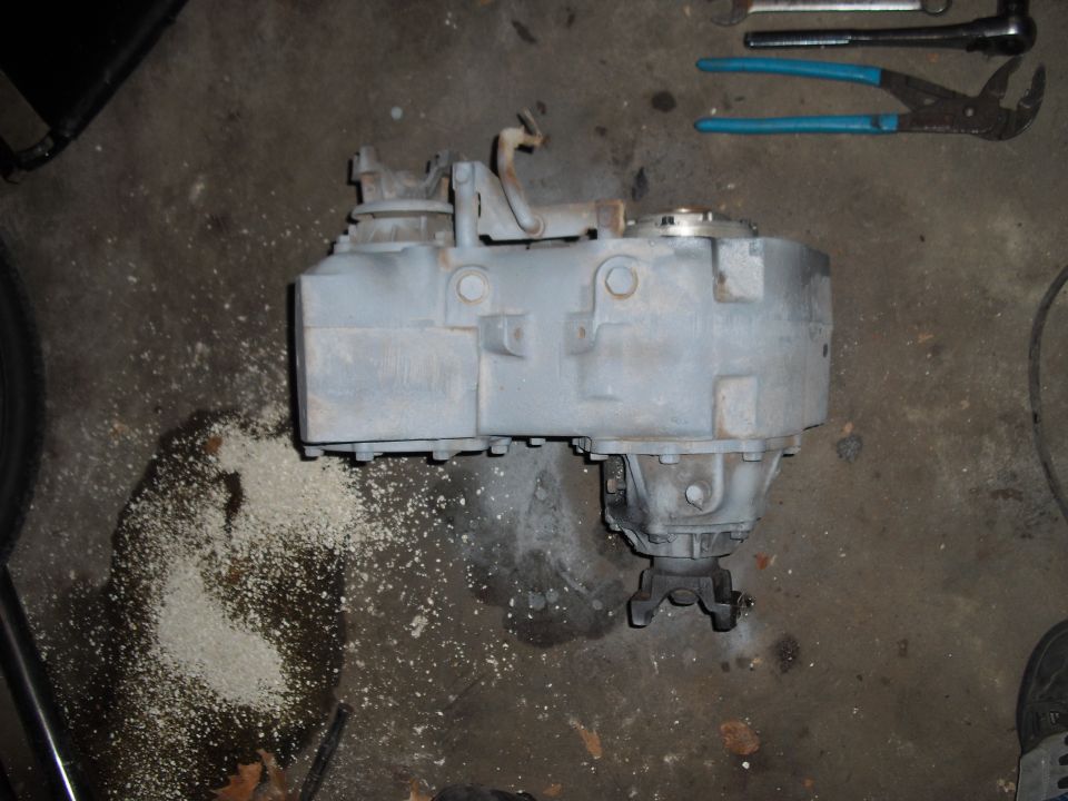 Gray transfer case on concrete floor with tools and debris