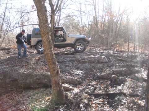 2005 Jeep Wrangler - A Jeep Wrangler navigates a rocky trail in a wooded environment, with a person observing nearby.