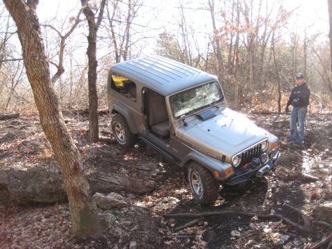 2005 Jeep Wrangler - A silver Jeep Wrangler navigates a challenging off-road course through a wooded area.