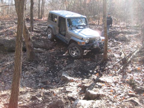 2005 Jeep Wrangler - A Jeep Wrangler is shown on a challenging off-road course with trees and rocks surrounding it.