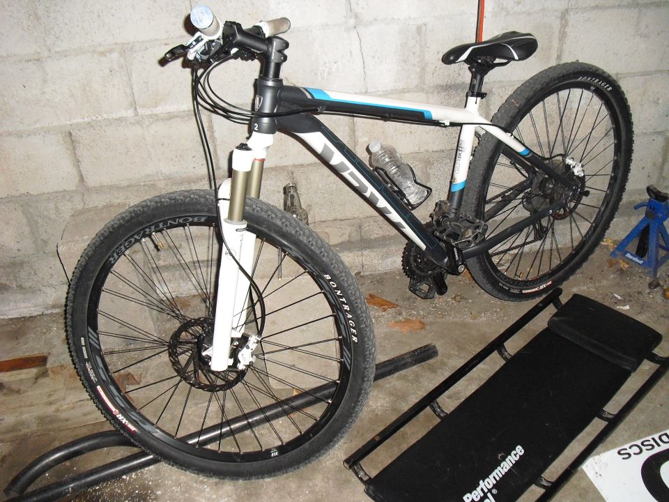 White and black mountain bike with blue accents on a stand, front wheel elevated