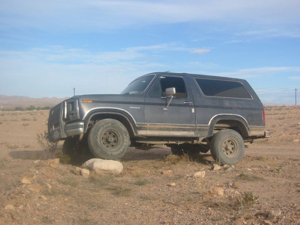 Dark Ford Bronco 2-door SUV parked side-on in dusty desert terrain