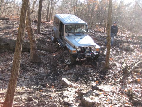 2005 Jeep Wrangler - A silver 2005 Jeep Wrangler tackles a challenging rocky path in a wooded area.