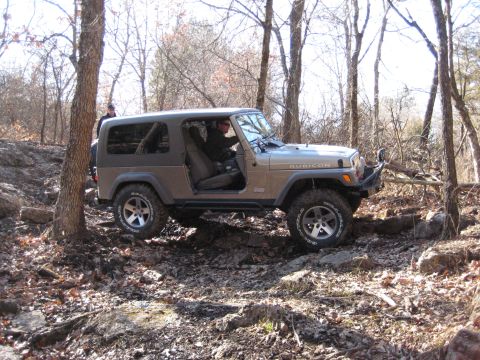 2005 Jeep Wrangler - A Jeep Wrangler Rubicon navigates a challenging off-road path through a wooded area with rocky terrain.