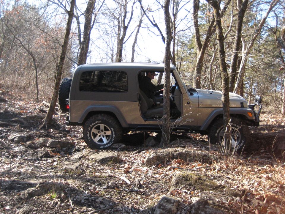 Tan Jeep Wrangler driving on a rocky, wooded trail