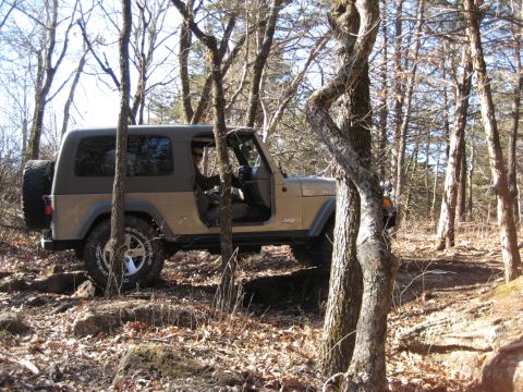 2005 Jeep Wrangler - A tan 2005 Jeep Wrangler navigates a rocky path through a wooded area.