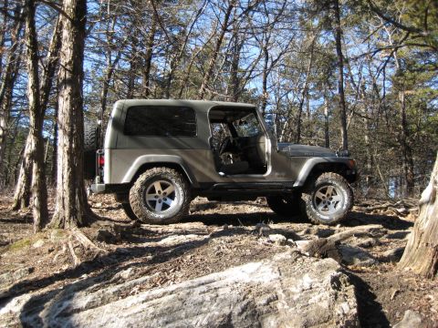 2005 Jeep Wrangler - A Jeep Wrangler navigates a rocky, wooded terrain on a clear day.