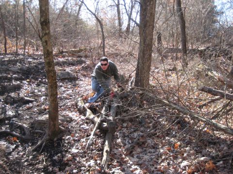 2005 Jeep Wrangler - A man crouches in a wooded area, surrounded by fallen leaves and branches.