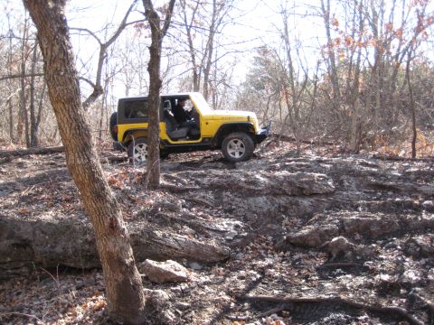 2005 Jeep Wrangler - A yellow Jeep Wrangler navigates a rocky trail through a forest with bare trees.