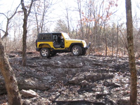 2005 Jeep Wrangler - A yellow Jeep Wrangler Rubicon navigates a rocky trail through a wooded area.