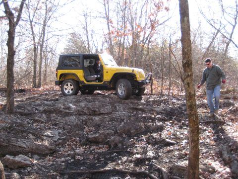 2005 Jeep Wrangler - A yellow 2005 Jeep Wrangler navigates a rocky, wooded path with two people visible inside.