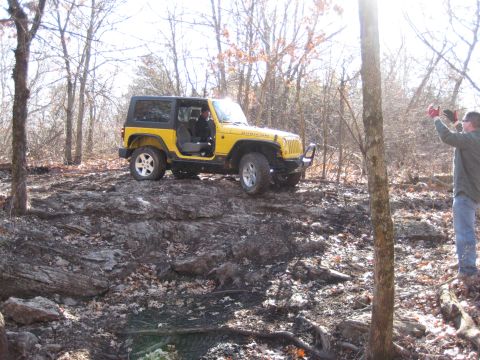 2005 Jeep Wrangler - A yellow 2005 Jeep Wrangler Rubicon navigates a challenging rocky incline in a forest.