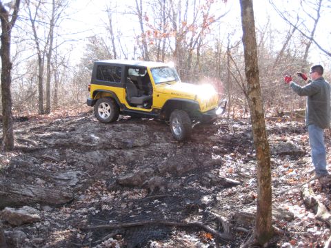 2005 Jeep Wrangler - A yellow Jeep Wrangler navigates a challenging off-road terrain in a wooded area.