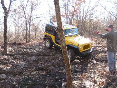 2005 Jeep Wrangler - A yellow Jeep Wrangler navigates a challenging off-road course in a wooded area.