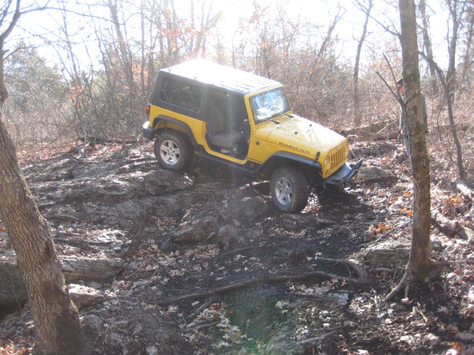 Yellow 2005 Jeep Wrangler Rubicon off-roading on a rocky, wooded trail