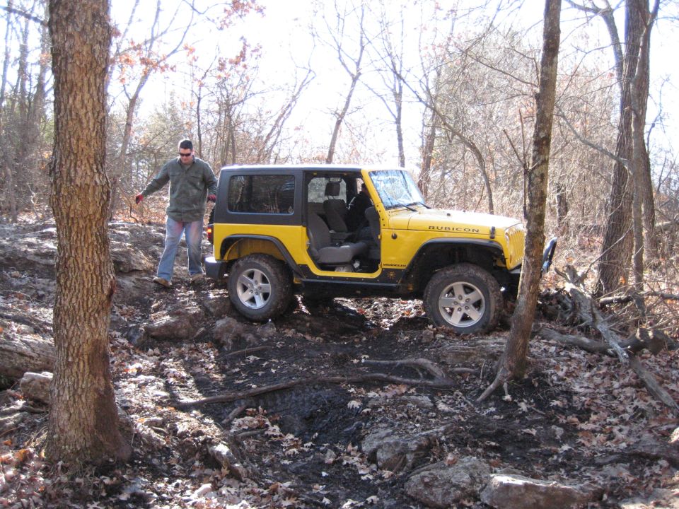 Yellow Jeep Wrangler Rubicon with doors removed, parked on a rocky, wooded trail