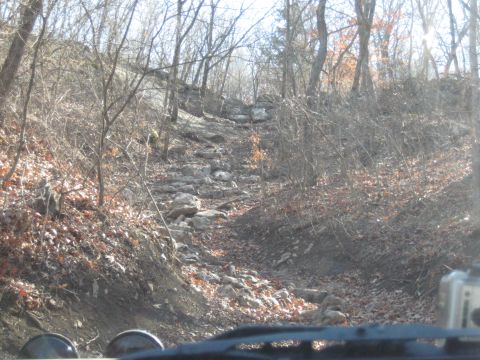 2005 Jeep Wrangler - The front view from inside a Jeep Wrangler shows a challenging rocky path ahead through a bare forest.