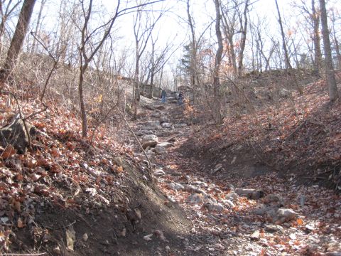 2005 Jeep Wrangler - A group of people navigate a challenging, rocky path through a wooded area.